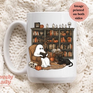 May include: White ceramic mug with a black cat and a ghost reading a book in a library setting. The ghost is sitting in a chair with a book in its hand. The cat is sitting on the floor next to the chair. The library has bookshelves filled with books and a few pumpkins on the shelves. The mug is printed on both sides.