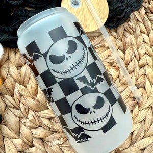 May include: A frosted glass water bottle with a black and white checkered pattern and a repeated image of Jack Skellington's face from the Nightmare Before Christmas. The bottle has a black lid and a clear straw.