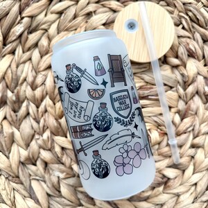 May include: A white frosted tumbler with a black and white design featuring a variety of illustrations including a potion bottle, a sword, a feather, a book, a crown, a lemon, and the text "I will not die today". The tumbler has a bamboo lid with a straw.