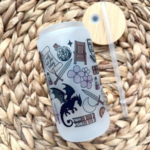 May include: A frosted glass tumbler with a straw and a lid. The tumbler has a white background with a black dragon, a sword, a crown, a book, and the text "I will not die today".