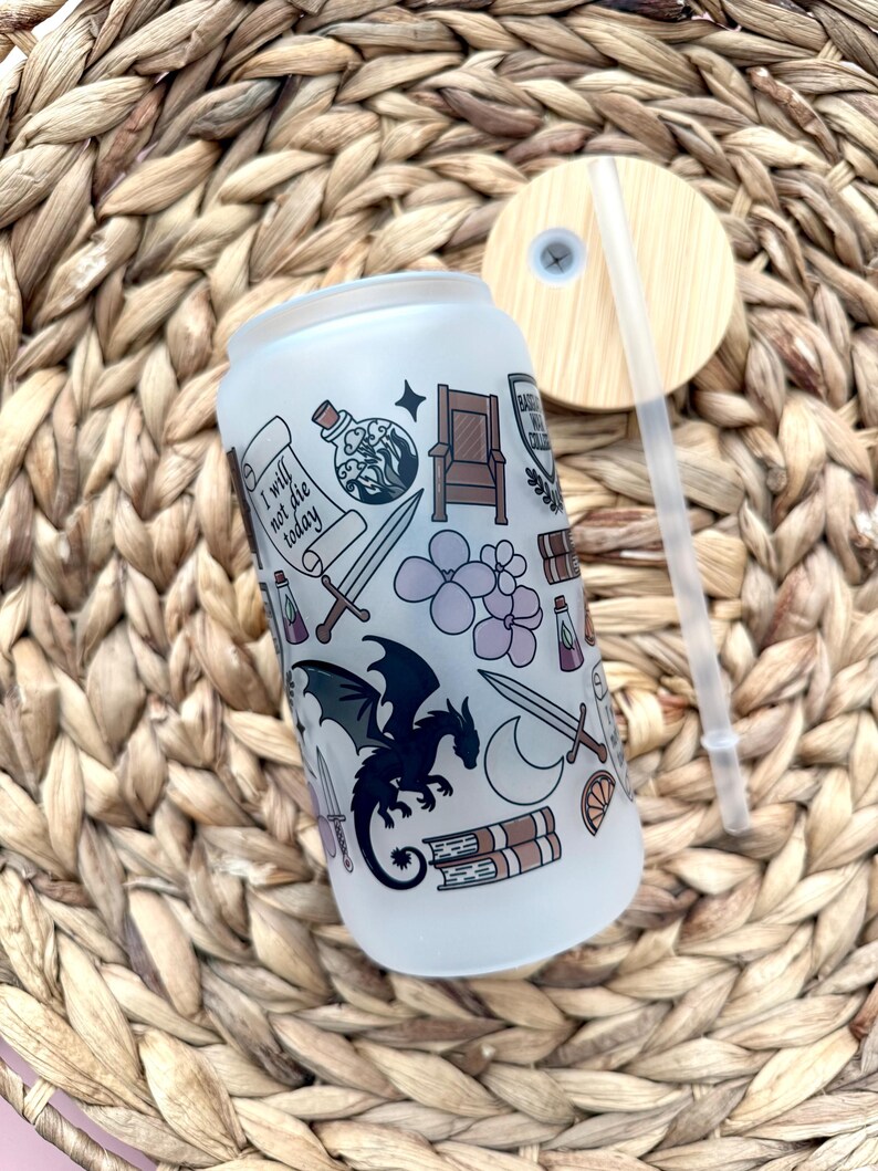 May include: A frosted glass tumbler with a straw and a lid. The tumbler has a white background with a black dragon, a sword, a crown, a book, and the text "I will not die today".