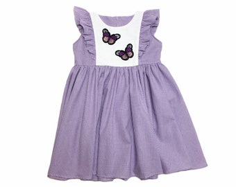 May include: A purple and white gingham dress with butterfly appliques. The dress has a white bodice with two purple butterflies and a purple gingham skirt.