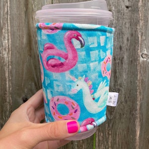 May include: A blue and pink fabric cup cozy with a flamingo, unicorn, and donuts. The cozy has the text "Seams Pretty" on the side.
