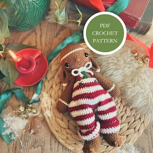 May include: A crocheted gingerbread man doll wearing red and white striped pants and a white bow tie. The doll is brown with black eyes and is lying on a woven mat. The image includes the text "PDF CROCHET PATTERN" in a green circle.