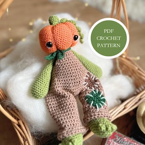 May include: A handmade crochet doll with a pumpkin head, green arms and feet, and brown overalls. The doll has black eyes and a green leaf collar. The doll is sitting in a wicker basket with a white fluffy material. The image includes a green circle with the text "PDF CROCHET PATTERN".