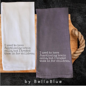 May include: Two kitchen towels, one white and one gray, are displayed on a wooden cutting board with a rope handle. Each towel has the text: "I used to have functioning brain cells, but I traded them in for children."