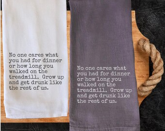 May include: Two kitchen towels, one white and one gray, with humorous text. The towels are displayed on a wooden cutting board with a rope handle. The text on the towels reads: "No one cares what you had for dinner or how long you walked on the treadmill. Grow up and get drunk like the rest of us."