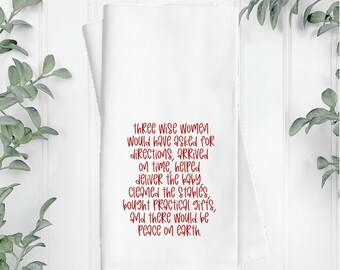 May include: A white rectangular kitchen towel featuring red text that reads: three wise women would have asked for directions, arrived on time, helped deliver the baby, cleaned the stables, bought practical gifts, and there would be peace on earth.