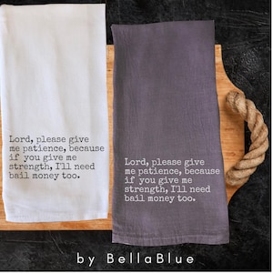 May include: Two kitchen towels, one white and one gray, with the text "Lord, please give me patience, because if you give me strength, I'll need bail money too." The towels are on a wooden cutting board with a rope handle. The brand name "Bella Blue" is at the bottom.