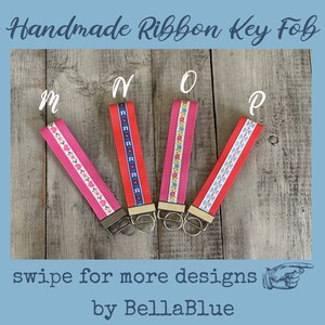 May include: Handmade ribbon key fobs in pink and red with floral and geometric patterns. Each fob has a metal clasp and key ring. The image includes the text "Handmade Ribbon Key Fob", "swipe for more designs", and "by BellaBlue".