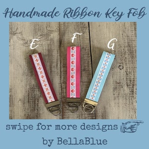 May include: Three handmade ribbon key fobs with different designs. One is burgundy with a white and orange pattern, another is pink with a floral pattern, and the third is light blue with a white and orange pattern. The text "Handmade Ribbon Key Fob" is at the top.