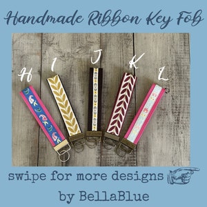 May include: Handmade ribbon key fobs in various designs. The key fobs feature colorful patterns, including floral and leaf motifs. Each fob has a metal clasp and key ring. The text "swipe for more designs" is visible.