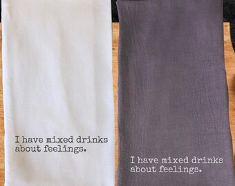 May include: Two kitchen towels, one white and one gray, are displayed side-by-side. Each towel has the phrase "I have mixed drinks about feelings" printed in black. The towels are made of a soft fabric.