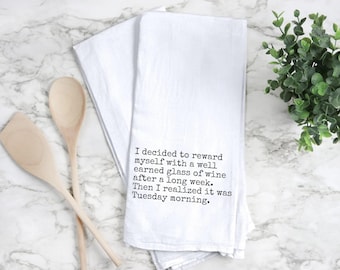 May include: White kitchen towel with the text "I decided to reward myself with a well earned glass of wine after a long week. Then I realized it was Tuesday morning." Two wooden spoons are on the left.
