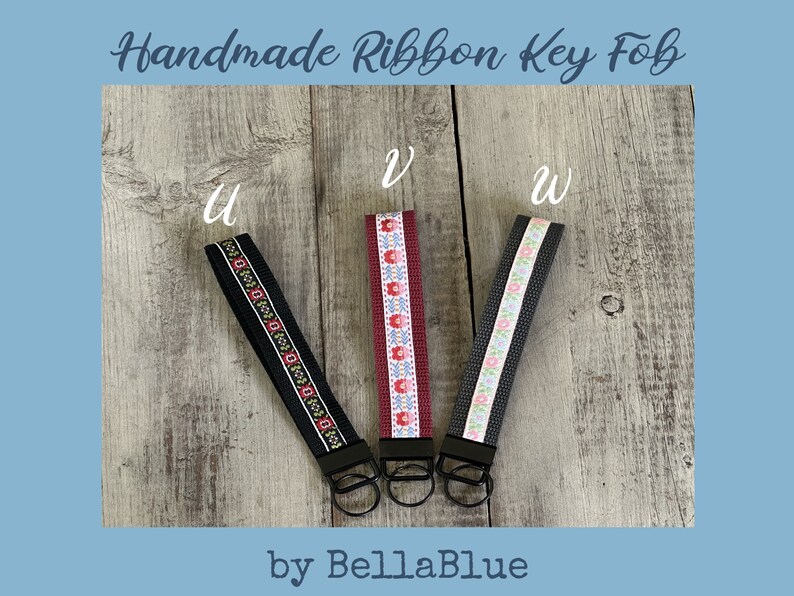 May include: Three handmade ribbon key fobs with black metal hardware. The key fobs have different ribbon designs: black with a red and white pattern, burgundy with a floral pattern, and gray with a floral pattern. The text "Handmade Ribbon Key Fob" and "by BellaBlue" are visible.