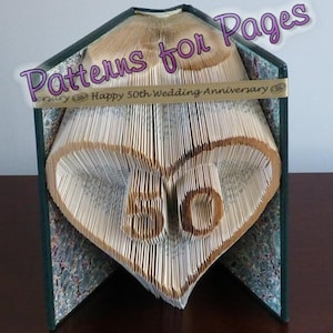 Puede incluir: Un libro con las páginas dobladas en forma de corazón con el número 50 en su interior. El libro está decorado con una cinta dorada que dice "Feliz 50 aniversario de boda". El libro se titula "Patterns for Pages".