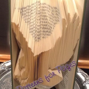 May include: A book with pages folded into a 3D design, creating a bird shape. The book is on a silver tray and the text "Patterns for Pages" is visible on the book.