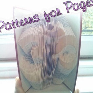 Puede incluir: Un libro doblado en una forma tridimensional, creando un diseño que se asemeja al símbolo Om. El libro está abierto y las páginas están dobladas en un patrón complejo. El título "Patterns for Pages" está escrito en letras rosas en la parte superior de la imagen.