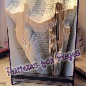 Puede incluir: Un libro con las páginas dobladas en un diseño 3D, creando un patrón de una persona. El libro está de pie sobre una mesa. El texto "Patterns for Pages" está escrito en morado en el libro.