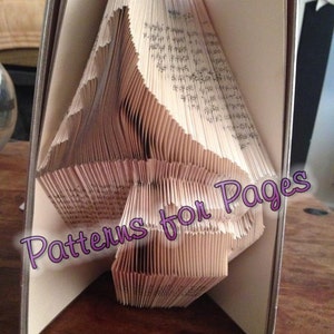May include: A book folded into a three-dimensional shape, creating a design of a bird. The book is open and the pages are folded in a way that creates a layered effect. The text "Patterns for Pages" is visible on the book.