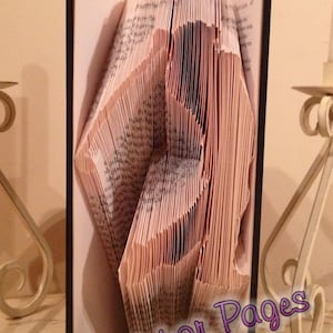 May include: A book with pages folded into a 3D design of a person. The book is standing upright on a table. The text "Patterns for Pages" is visible at the bottom of the image.