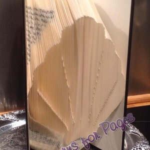 May include: A decorative book with pages folded into a seashell design. The book is beige with a black spine and is displayed on a silver tray. The text "Patterns for Pages" is visible on the book.