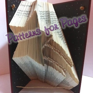May include: A book art sculpture with a star-shaped design, folded from the pages of a book. The book is bound in a dark red cover with a black spine. The sculpture is titled "Patterns for Pages" in purple text.
