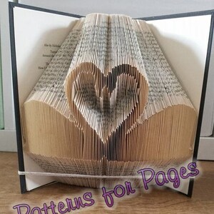 May include: A book with pages folded into a heart shape. The book is closed and has a black cover. The text "Patterns for Pages" is written in purple at the bottom of the image.