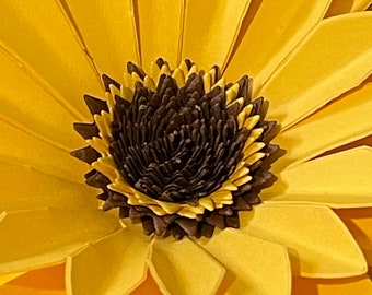 May include: A close-up of a large, yellow paper flower with a brown center. The flower is made of many layers of paper petals.