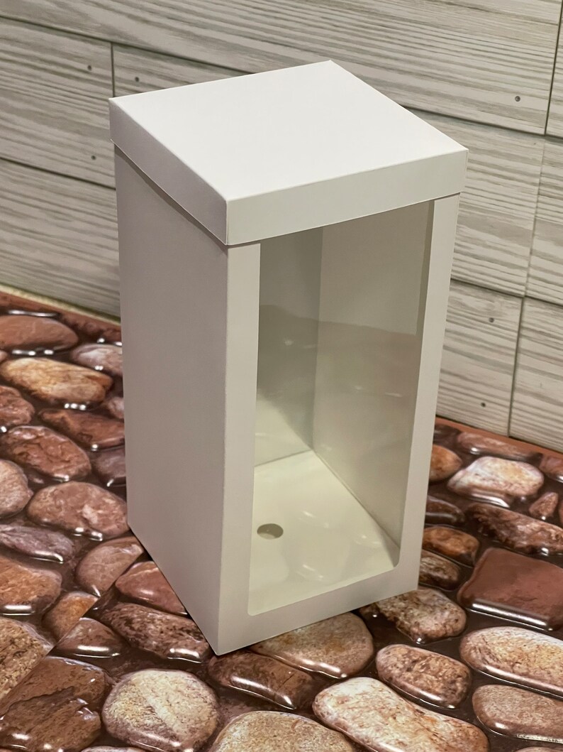 May include: White cardboard box with a clear plastic window on the front. The box has a hole in the bottom.