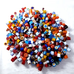 May include: A pile of colorful glass beads in various shapes and sizes. The beads are a mix of red, orange, yellow, blue, and white, with floral and star patterns. These beads are ideal for jewelry making and crafting.