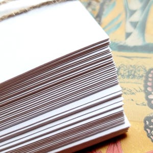 May include: A stack of white blank cards tied together with twine. The cards are arranged in a neat pile and are ready to be used for writing or crafting.