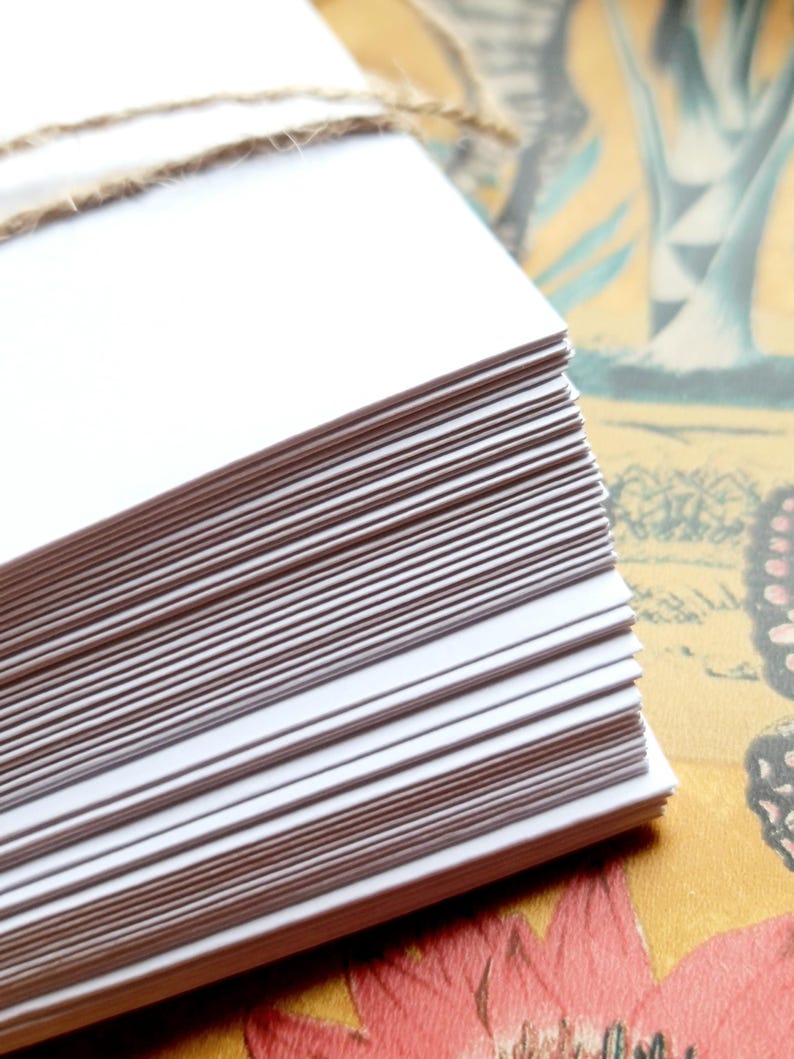 May include: A stack of white blank cards tied together with twine. The cards are arranged in a neat pile and are ready to be used for writing or crafting.