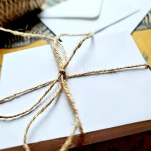 May include: A stack of white blank note cards tied together with twine. The twine is tied in a bow on top of the stack.