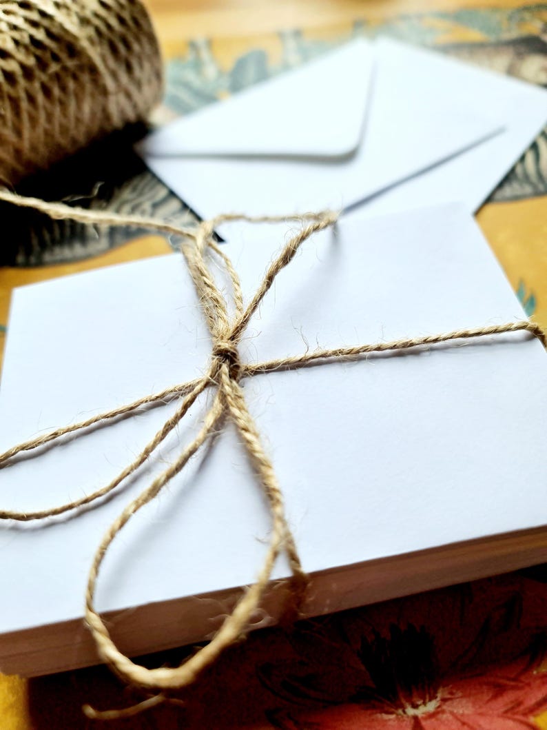 May include: A stack of white blank note cards tied together with twine. The twine is tied in a bow on top of the stack.