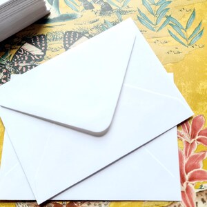 May include: Two white envelopes stacked on top of each other on a yellow and green patterned surface. The envelopes are blank and have a flap on the top.
