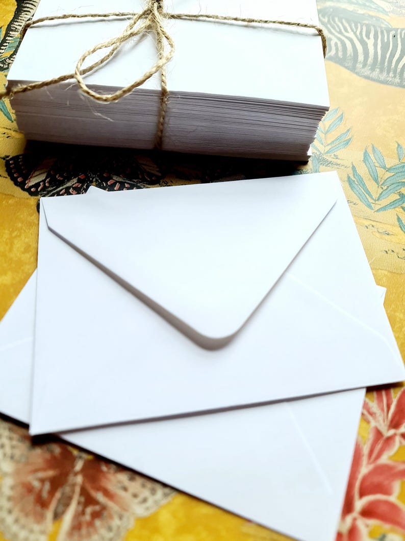 May include: A stack of white envelopes tied together with twine. The envelopes are on a colorful patterned surface.