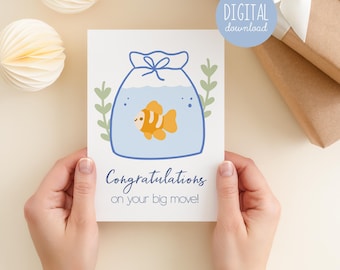 May include: A greeting card featuring a cartoon fish in a blue fishbowl. The card says "Congratulations on your big move!" and has a "DIGITAL download" sticker. The card is held by hands.