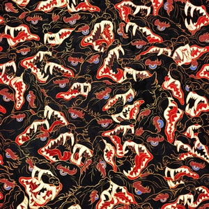 Op de afbeelding: Een herhalend patroon van zwarte en witte wolfskopjes met rode en gouden accenten. De wolfskopjes zijn allemaal naar voren gericht met hun bek open en zichtbare tanden. De achtergrond is zwart.