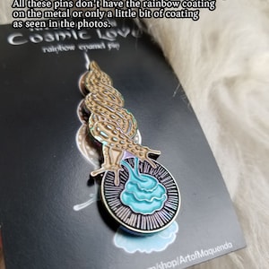 Op de afbeelding: Een Cosmic Love regenboog emaille pin met een slakachtig wezen met een lichtbruine schaal en blauwe vloeistof. De pin zit op een zwarte kaart met tekst.