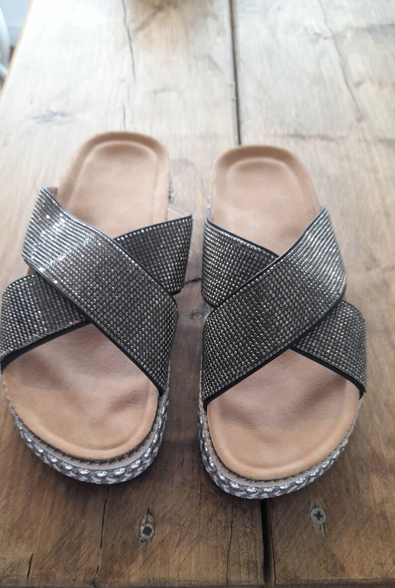 Puede incluir: Un par de sandalias negras con un dise&ntilde;o de correa cruzada. Las correas est&aacute;n cubiertas de diamantes de imitaci&oacute;n.