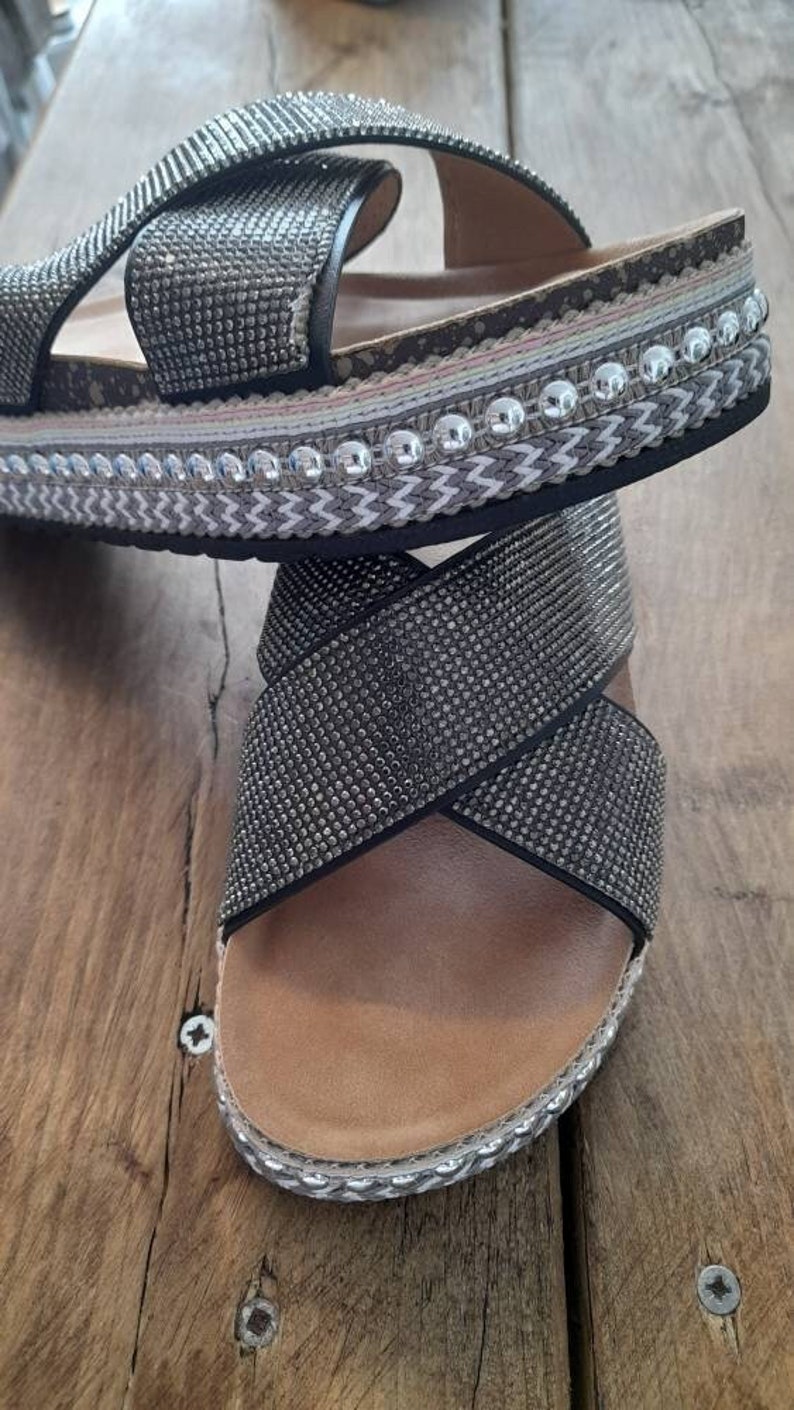 Puede incluir: Sandalias negras con dise&ntilde;o de tiras cruzadas. Las tiras est&aacute;n cubiertas de pedrer&iacute;a y las sandalias tienen una suela de plataforma con un ribete decorativo.