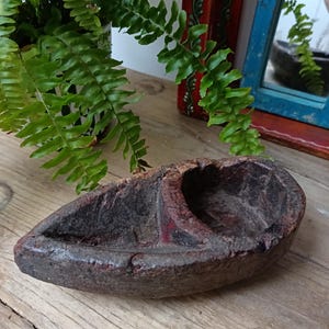 May include: A weathered, dark brown wooden bowl with two sections. The bowl has an aged appearance, with visible grain and a rough texture. The shape is elongated and boat-like, suggesting a vintage or rustic aesthetic. The bowl is likely used for decorative or functional purposes.