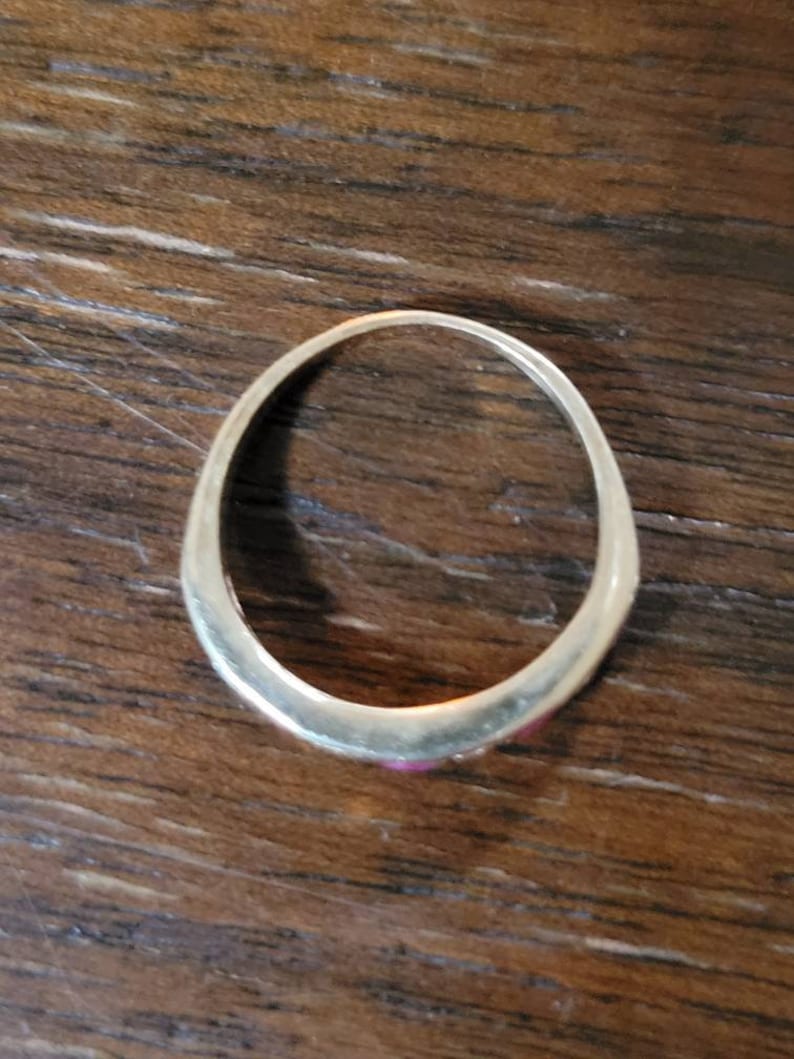May include: A gold band ring with three small pink stones set in the band.