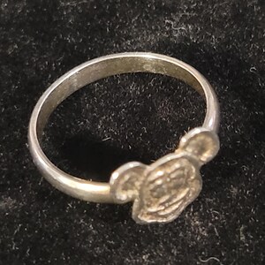 Pu&ograve; includere: Un anello color argento caratterizzato da un design in rilievo raffigurante la testa di un personaggio con due orecchie arrotondate. La fascia &egrave; liscia e circolare, con una finitura metallica che riflette la luce su tutta la superficie.