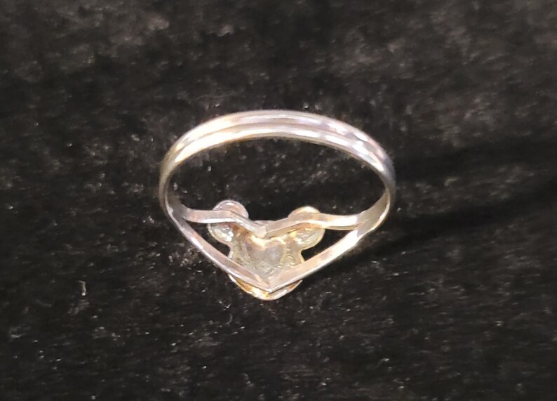 Puede incluir: Un anillo de tono plateado que presenta un dise&ntilde;o central con forma de cabeza de rat&oacute;n estilizada, con dos orejas circulares y una cara redondeada. La banda es delgada y met&aacute;lica, conect&aacute;ndose a la base del adorno en la parte frontal.