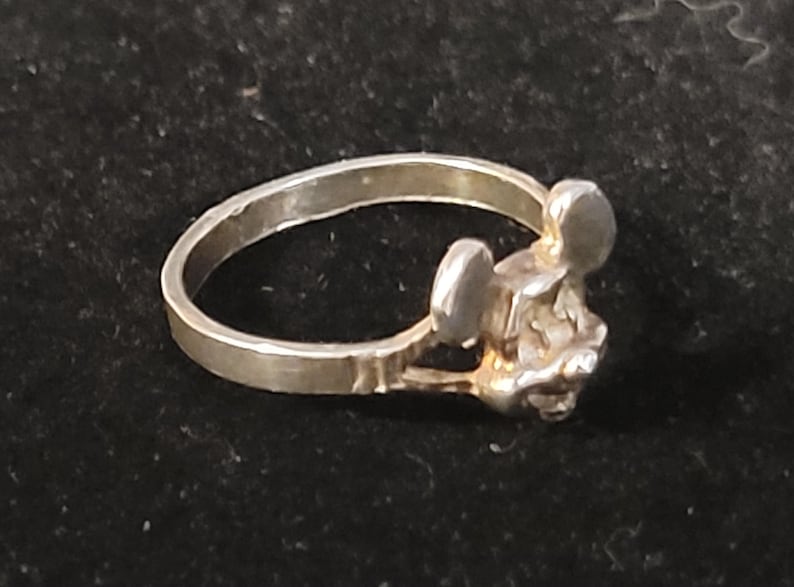 Puede incluir: Un anillo plateado con un dise&ntilde;o de rat&oacute;n estilizado. El anillo tiene una banda simple y una cabeza de rat&oacute;n detallada con orejas redondeadas. El anillo probablemente est&aacute; hecho de metal y es adecuado para el uso diario.