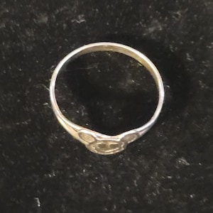 Puede incluir: Un anillo de metal plateado que presenta un elemento de dise&ntilde;o central con forma de cabeza de rat&oacute;n estilizada, con dos orejas circulares y una cara redondeada. La banda es delgada y circular, manteniendo un acabado met&aacute;lico uniforme.