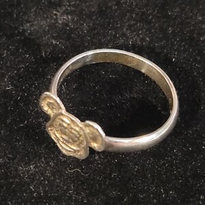 Pu&ograve; includere: Un anello in metallo color argento con una faccia piatta e circolare caratterizzata da un design in rilievo di una testa di topo dei cartoni animati con due orecchie arrotondate. La fascia &egrave; liscia e circolare, collegata alla base.