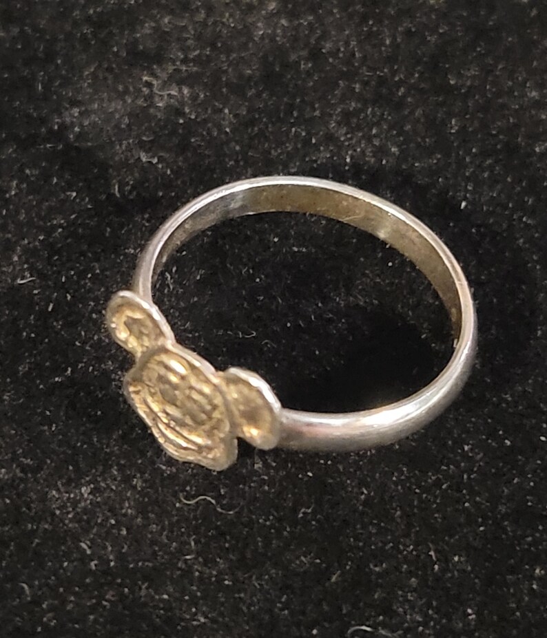 Pu&ograve; includere: Un anello in metallo color argento con una faccia piatta e circolare caratterizzata da un design in rilievo di una testa di topo dei cartoni animati con due orecchie arrotondate. La fascia &egrave; liscia e circolare, collegata alla base.